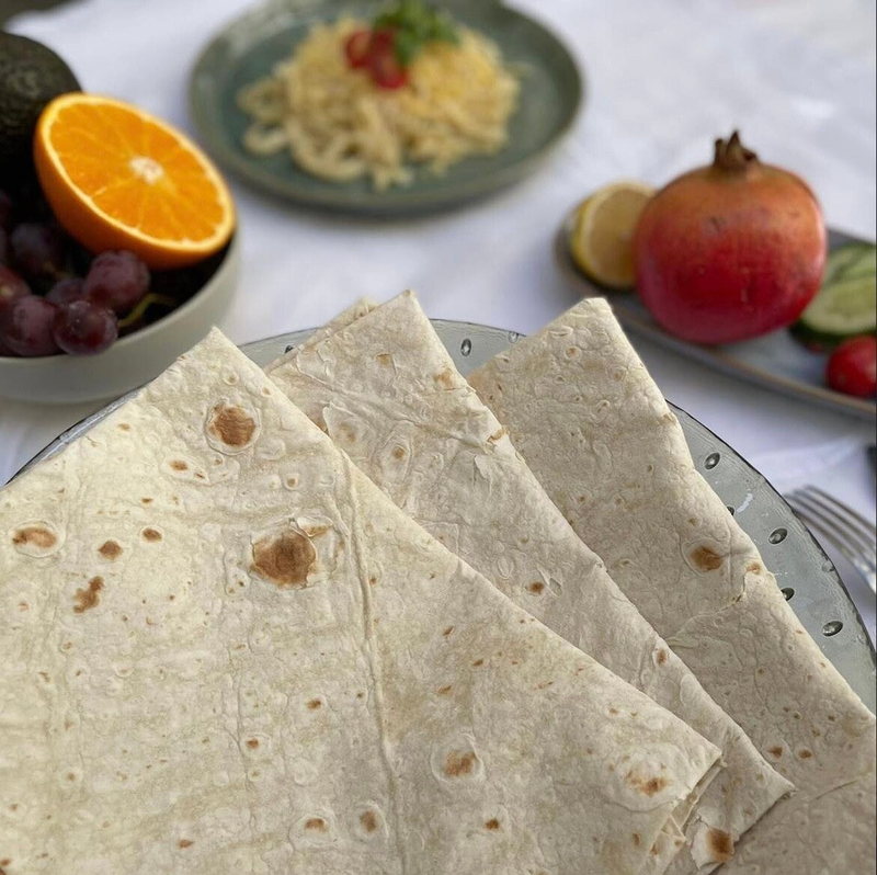 Gefaltete Köy Yufkası auf einer Glasschale, dahinter Orange, Granatapfel und Trauben auf einer weißen Tischdecke
